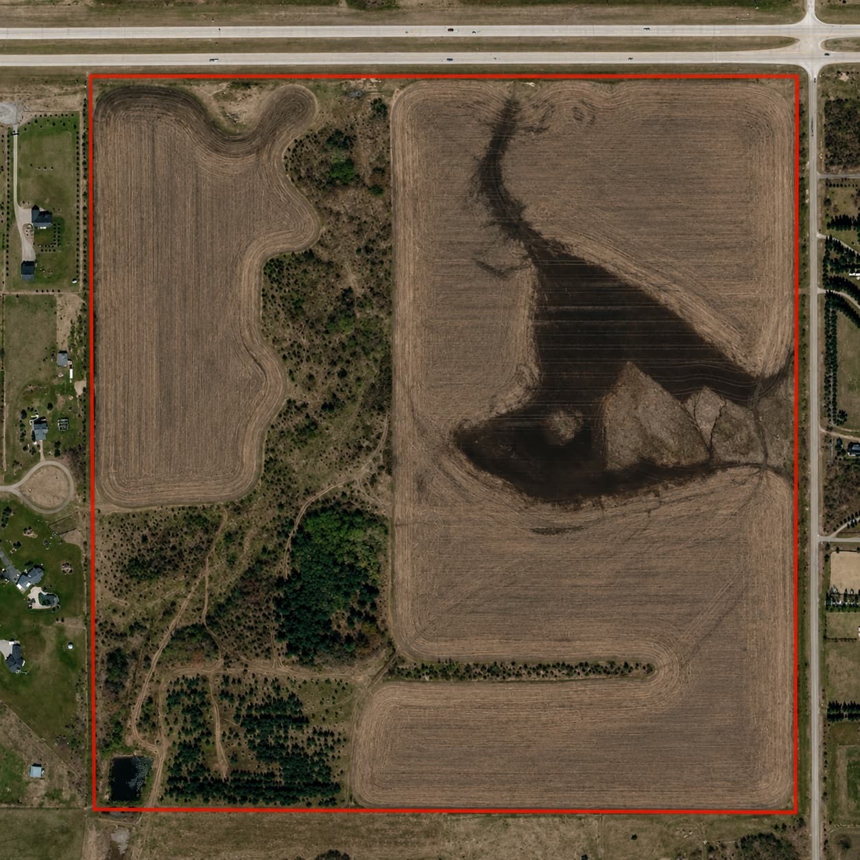 Aerial view of the Stonebridge lands in Foothills County, a quarter section of cultivated field and tree cover outlined in red, with a highway along the north edge.