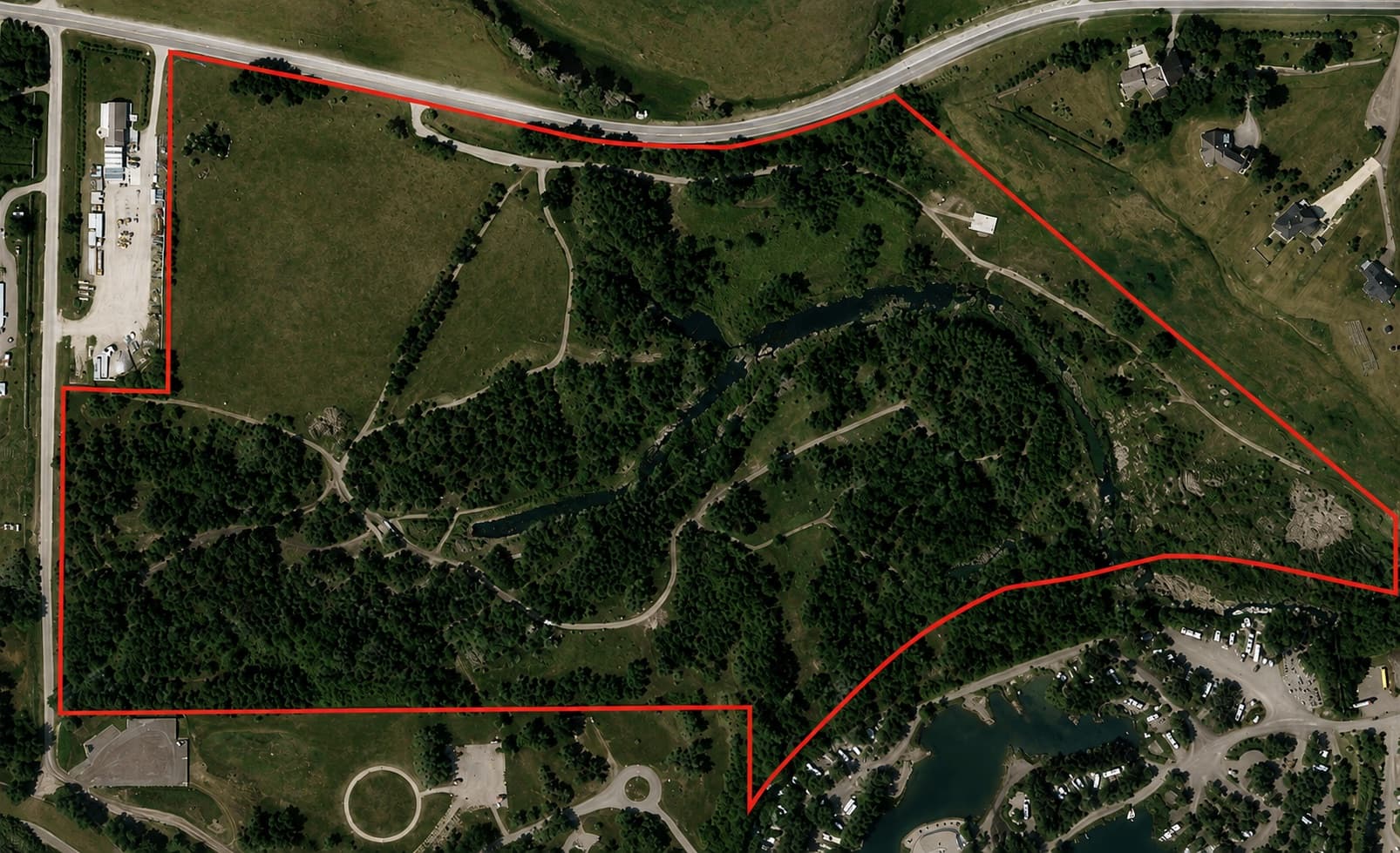 Aerial view of the Okotoks Wilderness Campground lands, a wooded river valley with campground roads and ponds, outlined in red.