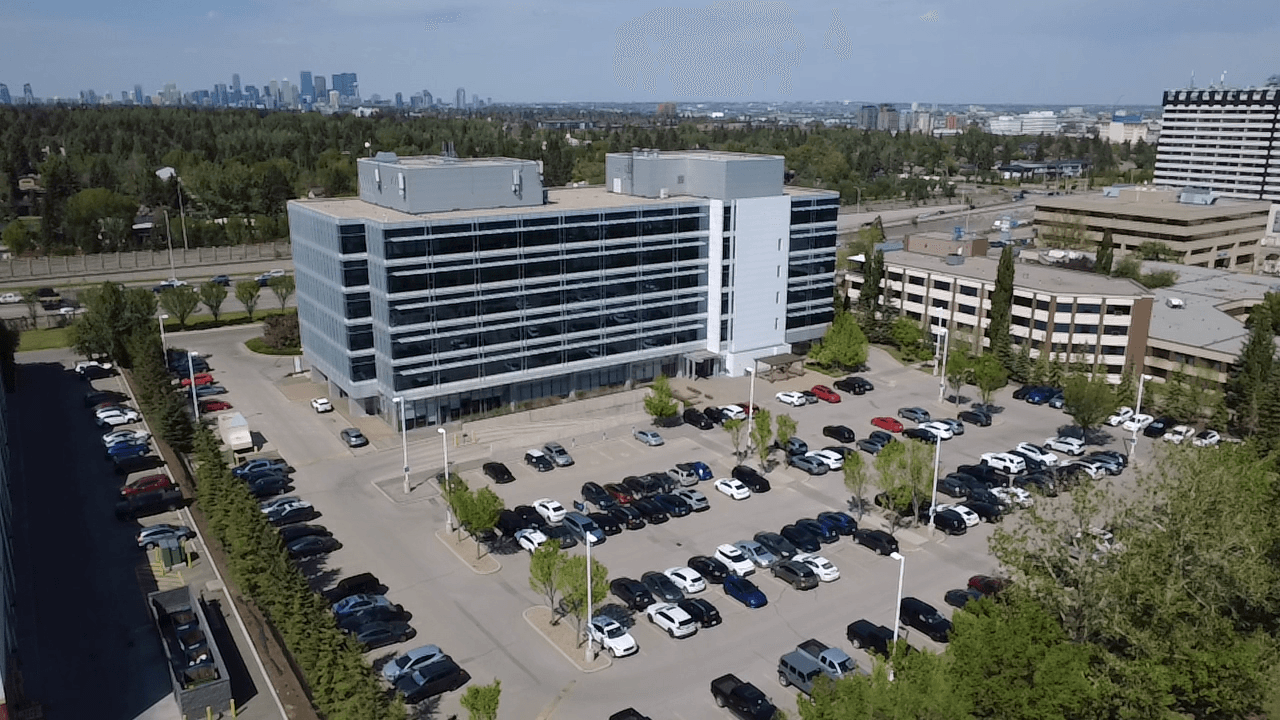 Aerial view of a multi-storey Calgary office building and its parking lot, with the downtown skyline on the horizon.