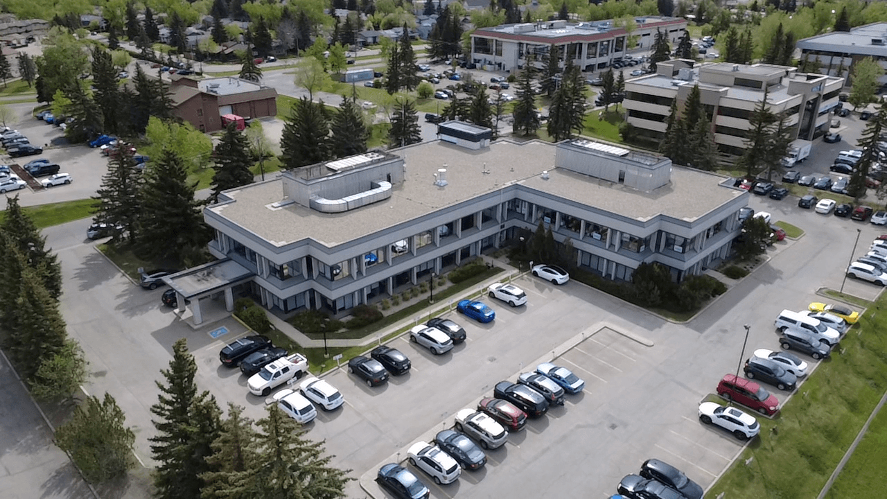 Aerial view of a low-rise Calgary commercial building surrounded by parking and mature trees.